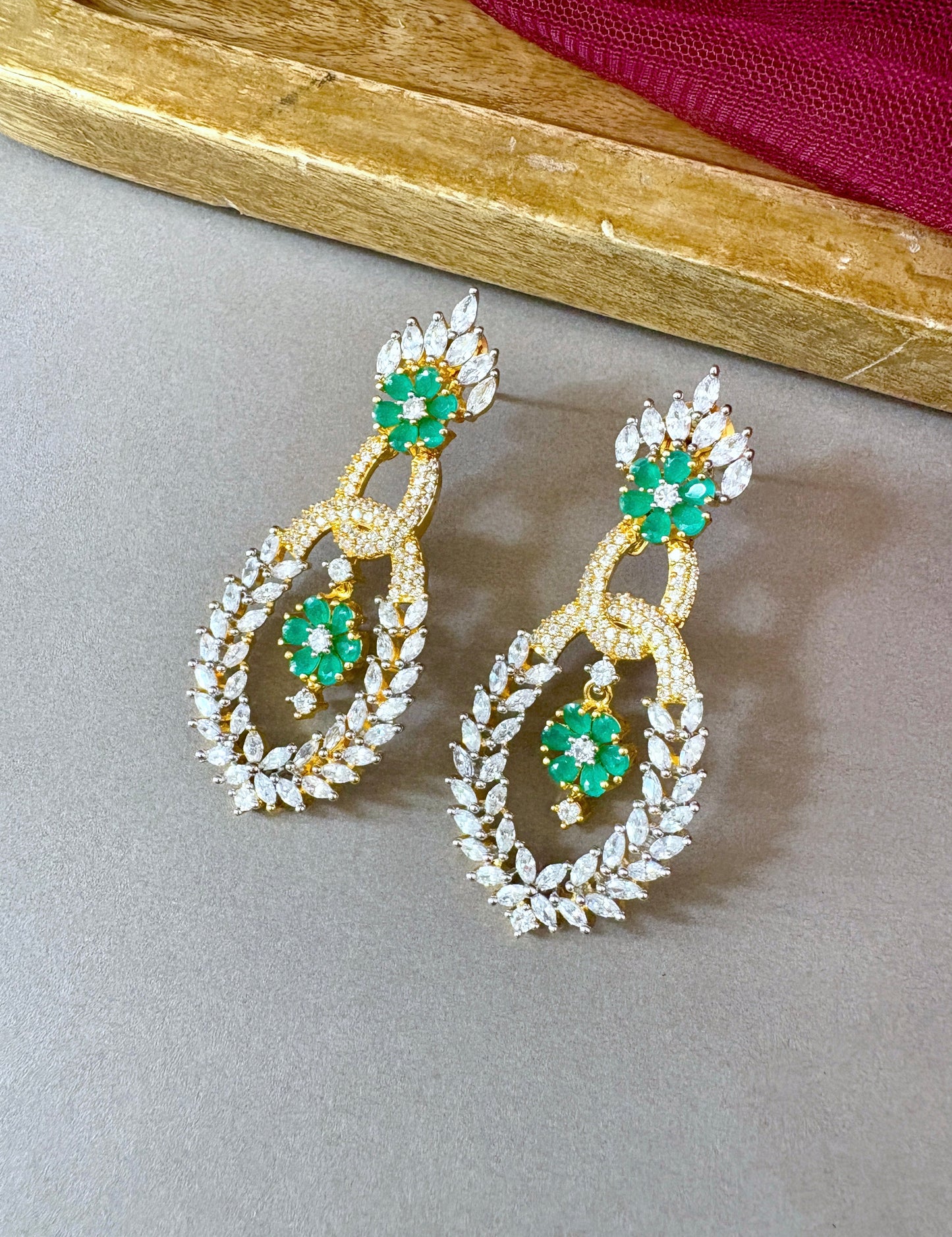 Pair of gold earrings with green gemstones on a gray surface