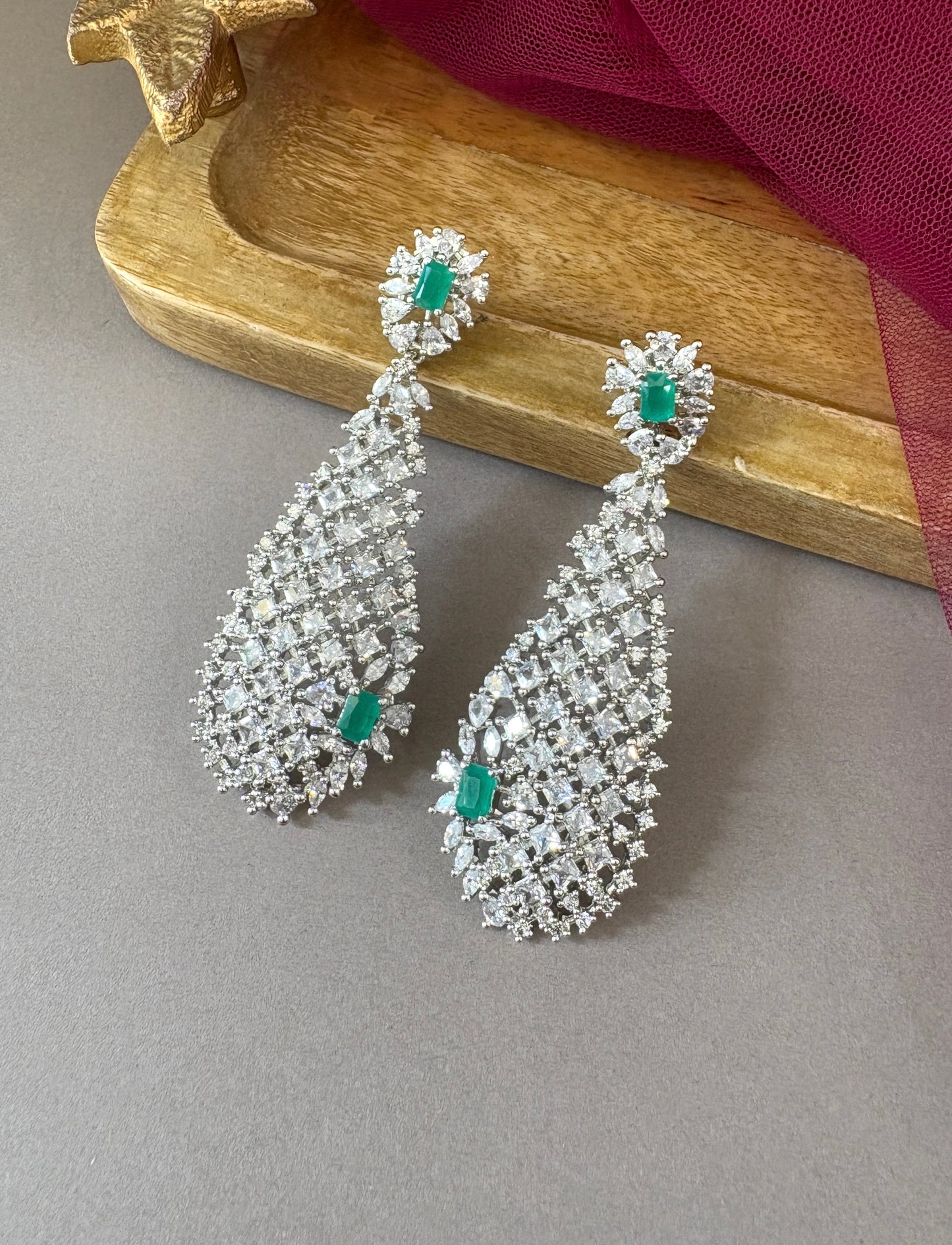 Teardrop-shaped earrings with emerald stones on a wooden surface