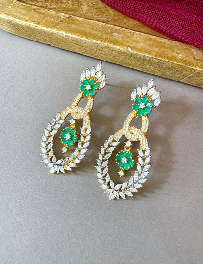 Pair of gold earrings with green gemstones on a gray surface