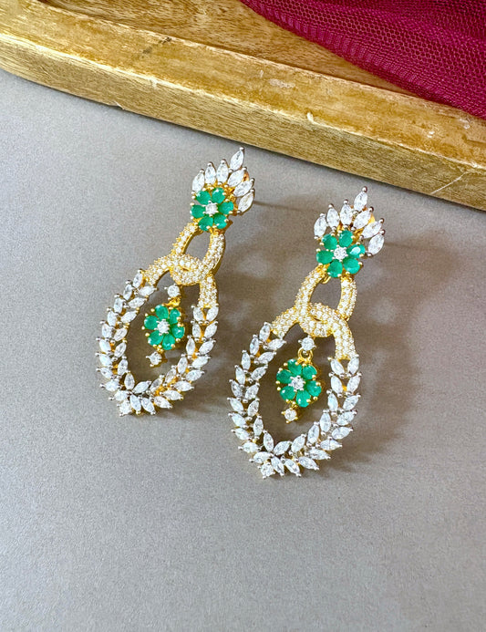 Pair of gold earrings with green gemstones on a gray surface